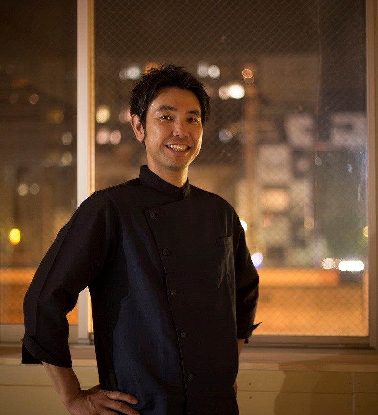 黒いコックコートを着て店に立つ、みんなの株式会社の料理人